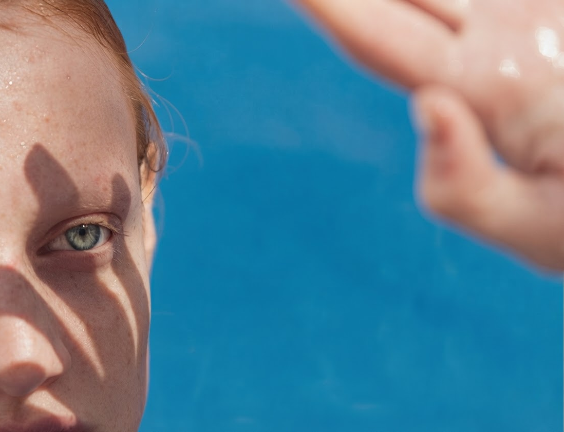 Sun-lit portrait of a woman shielding her eyes against a blue sky